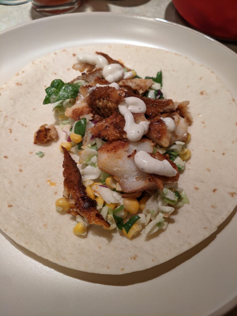 A very nice fish taco composed of a cabbage and corn slaw, wonderfully pan fried Pacific cod, and garlic sauce on top of a flour tortilla.